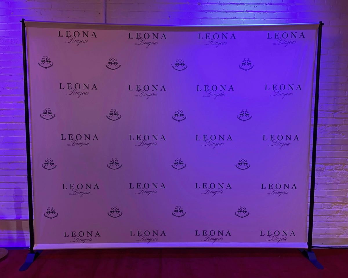 Leona Lingerie logo step-and-repeat backdrop on a stand under purple event lighting: custom photo booth backdrop rental in Brampton
