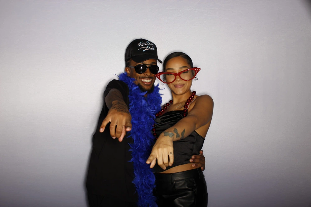 A man and a woman pointing at the camera while wearing props like a feather boa and sunglasses, highlighting a fun photo booth rental experience.