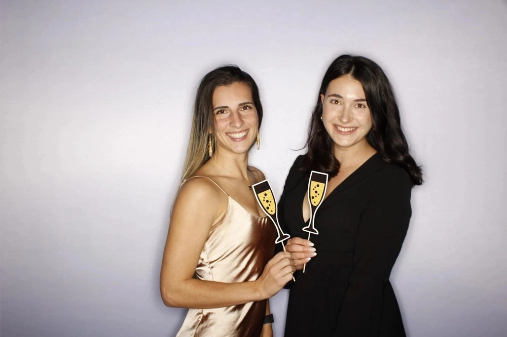 Two women in party attire smiling and holding champagne glass props, showcasing the fun and celebratory atmosphere of a photo booth rental in Mississauga.